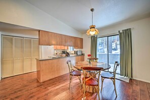 Une cuisine moderne avec un îlot central en bois, une table à manger avec des chaises et une vue sur l’extérieur grâce à de grandes fenêtres.