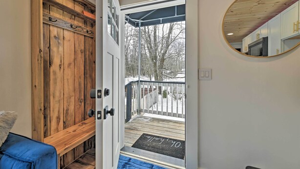 Eine Holztür führt zu einem Deck mit Fußmatte, einem Spiegel an der Wand und einer blauen Bank.