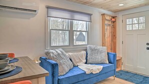 Ein gemütliches Zimmer mit einem blauen Sofa, einer Holztür und einem Fenster mit Blick auf Bäume.