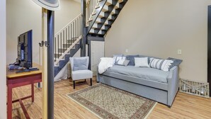 Una sala de estar con un sofá, una silla, un televisor sobre una mesa de madera, una escalera y un ventilador.