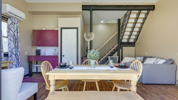 Un comedor con una mesa y sillas de madera, una cocina al fondo y una escalera que sube a otro nivel.
