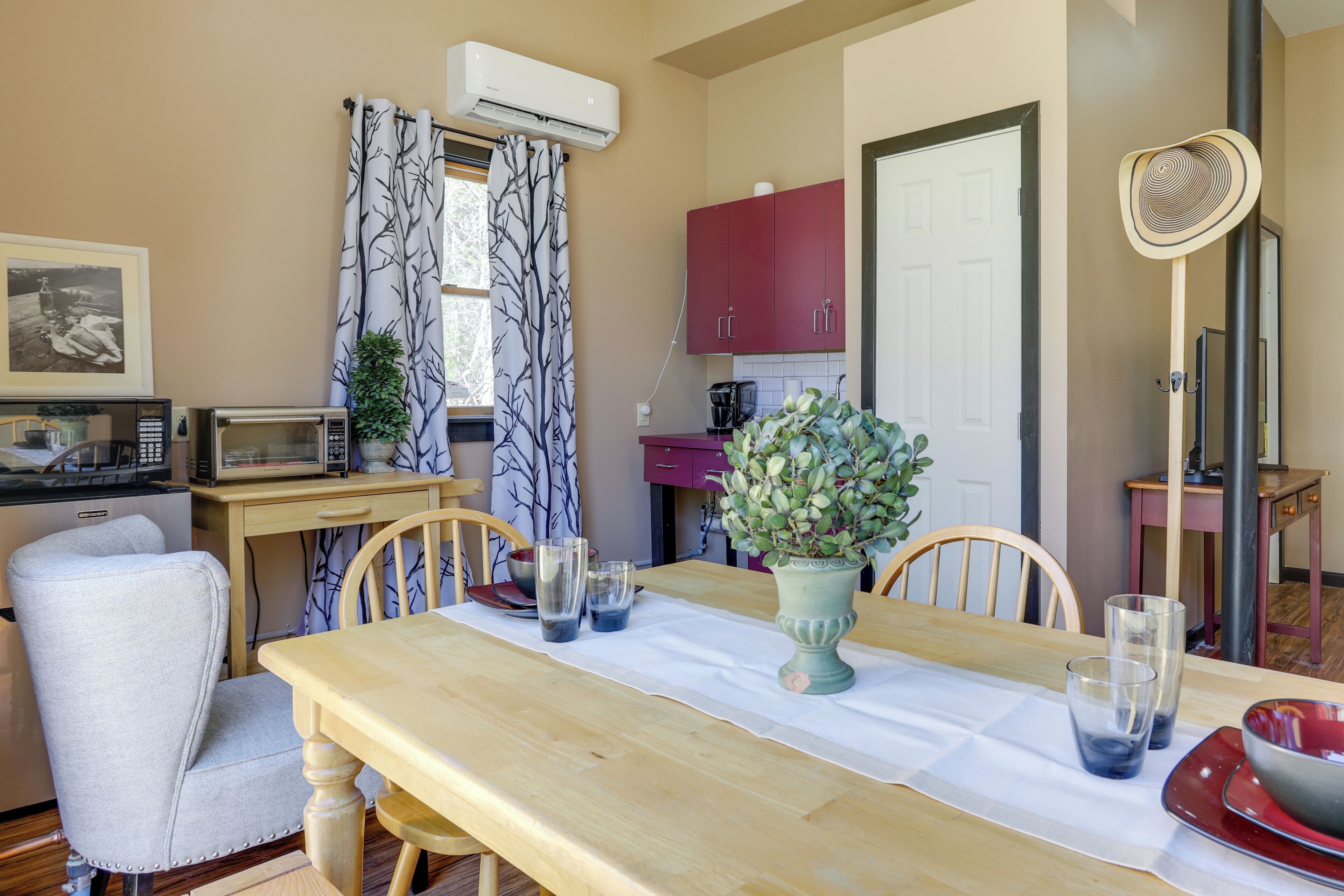 Un comedor con una mesa de madera, sillas, un jarrón de flores y un microondas.