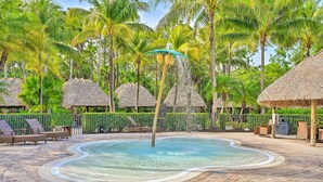 A pool area with a thatched-roof structure, lounge chairs, and a tropical setting with palm trees. - Naples Resort Townhome w/ Endless Amenities! (Naples)