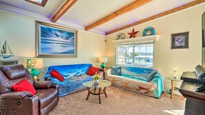 A cozy living room with a leather recliner, a blue sofa, a glass coffee table, and a large painting of a seascape.