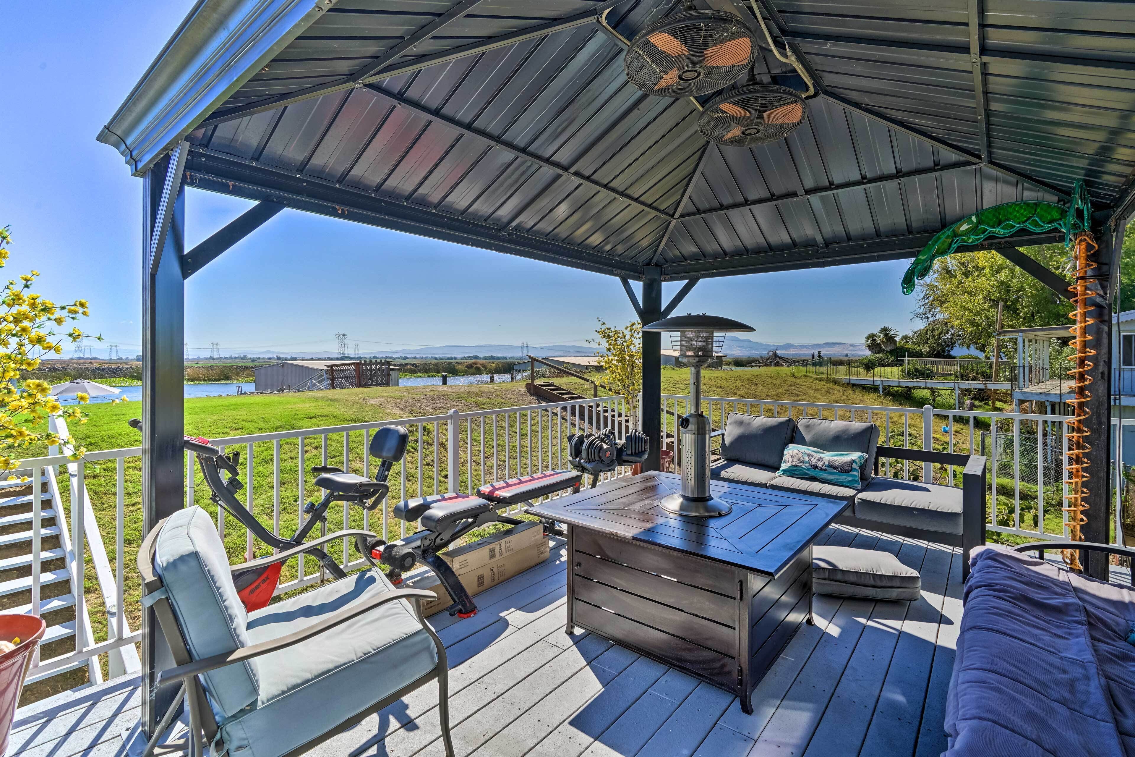Eine überdachte Terrasse im Freien mit Trainingsgeräten, Sitzmöglichkeiten und Blick auf die Landschaft.