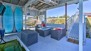 A covered outdoor patio with seating, surfboards, and a pool.