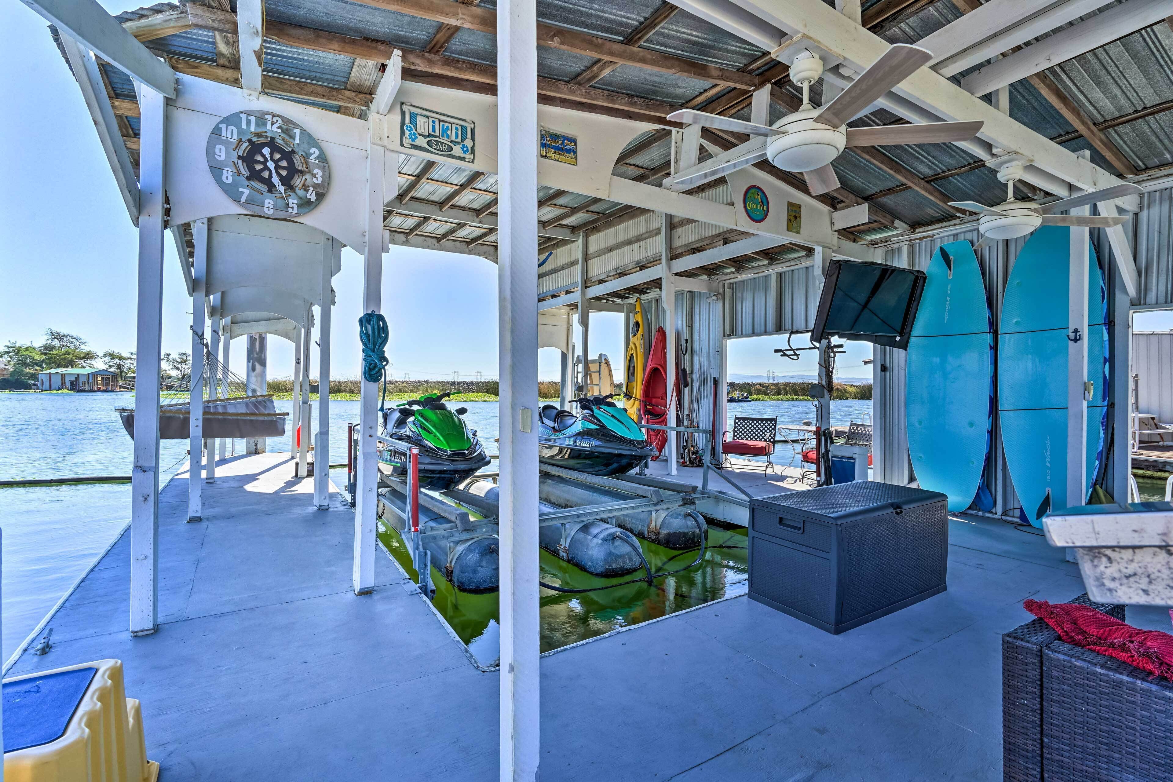 Een overdekt terras met een klok, zitplaatsen, surfplanken en jetski's.