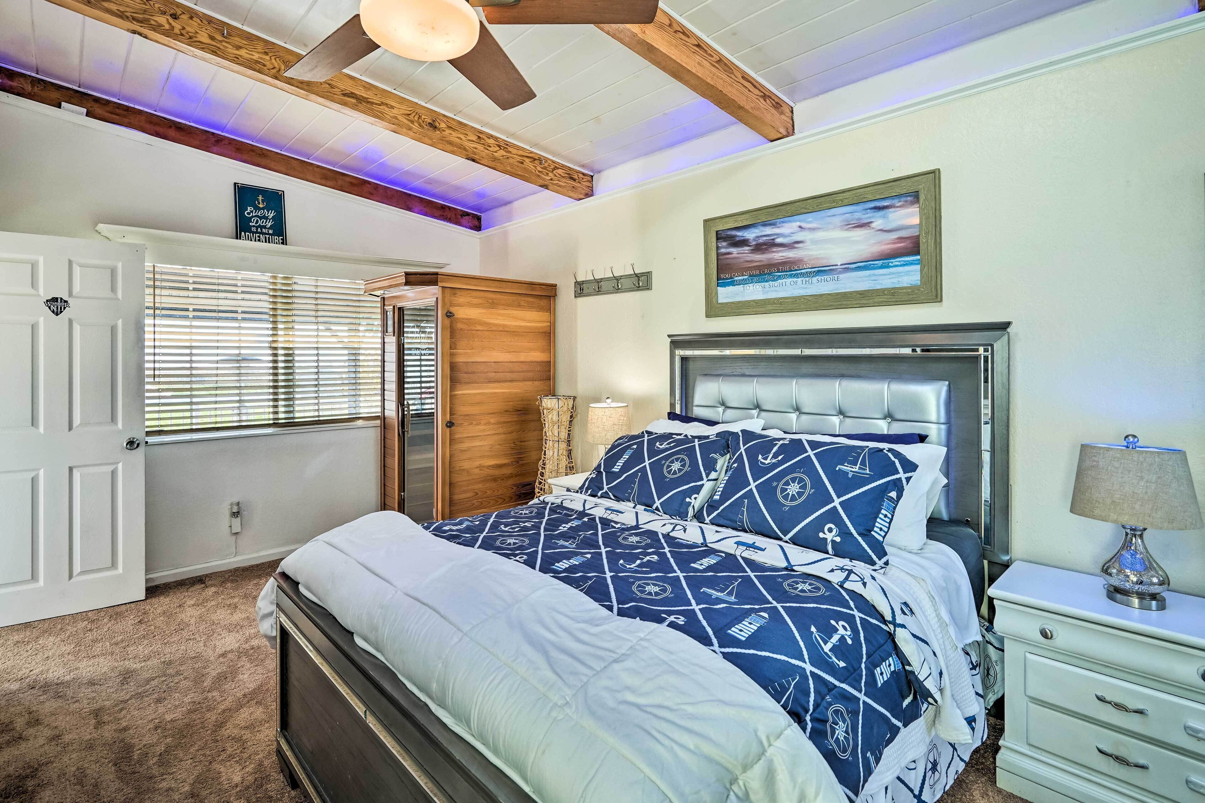 A bedroom with a bed, a nightstand, a lamp, a window with blinds, a door, and a ceiling fan.