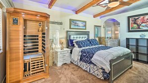 A bedroom with a wooden wardrobe, a bed with a blue and white patterned bedspread, a ceiling fan, and a large window.