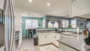 A modern kitchen with white cabinets, a stainless steel refrigerator, and a dining area with a table and chairs. - Avondale Getaway < 8 Mi to Estrella Mountain! (Avondale)