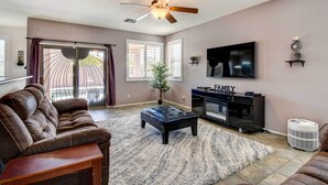 A living room with a brown leather sofa, a black ottoman, a ceiling fan, a flat-screen TV, and a fireplace. - Avondale Getaway < 8 Mi to Estrella Mountain! (Avondale)