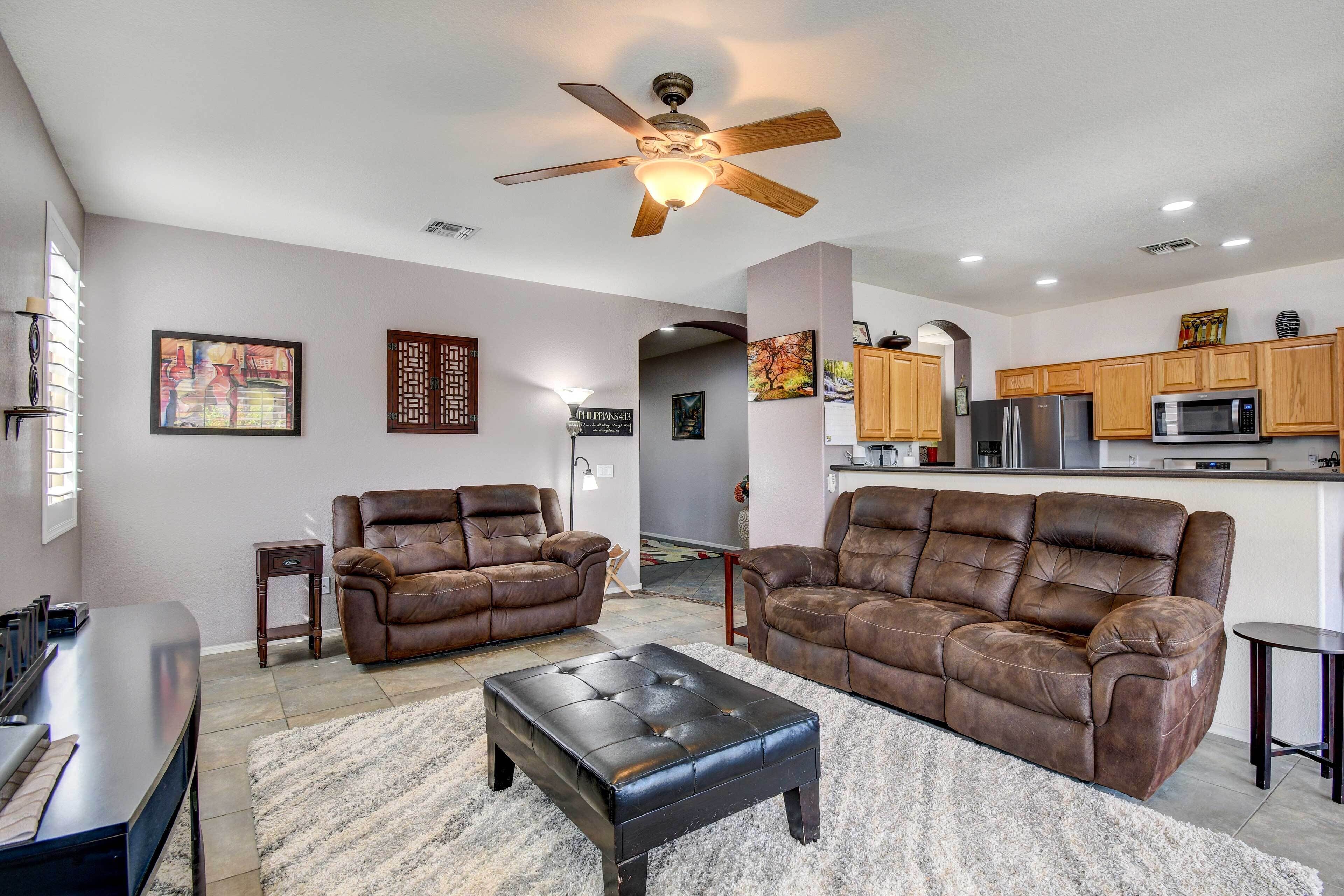 A living room with two brown leather sofas, a black ottoman, and a ceiling fan.