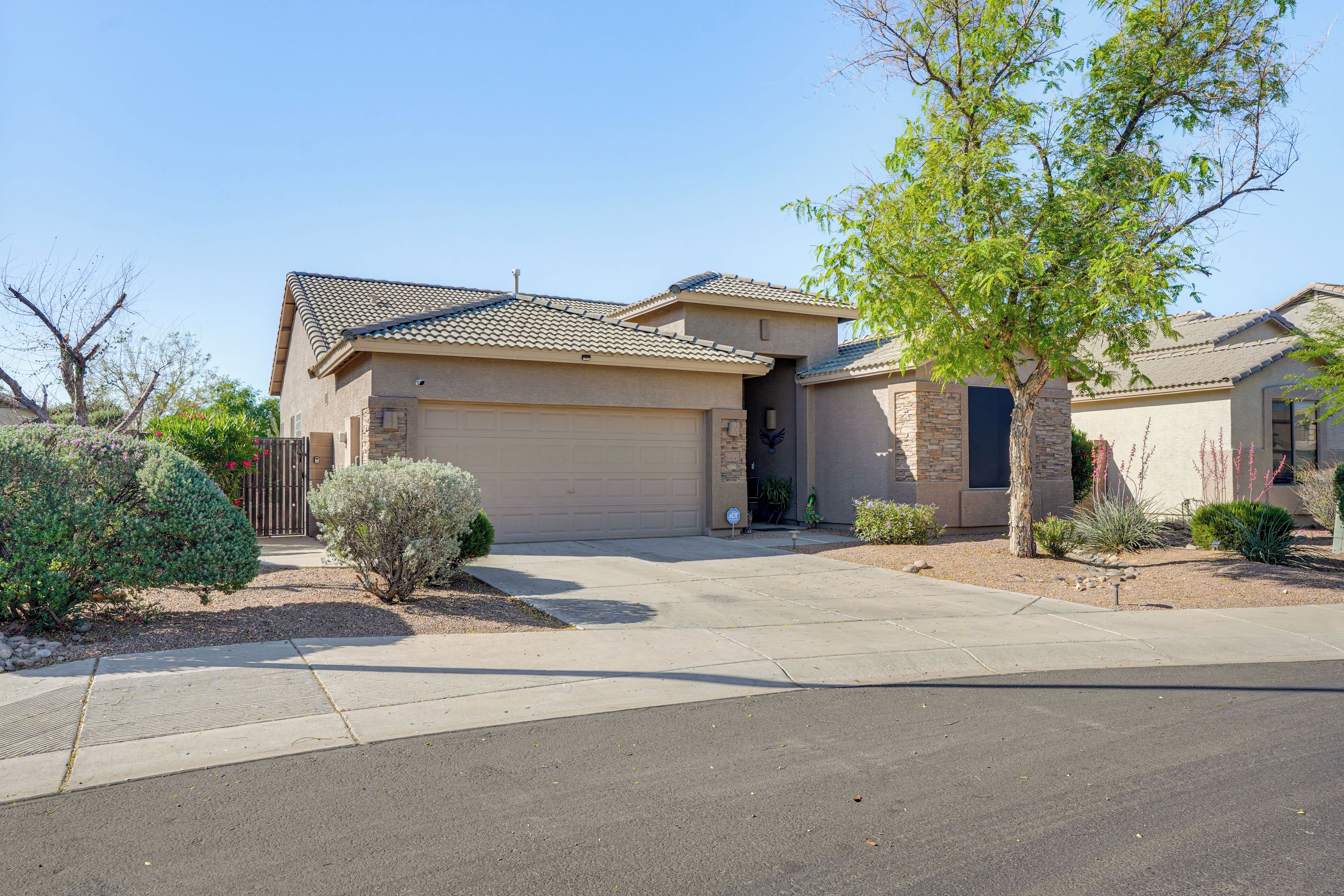 A two-story house with a garage, a driveway, and a well-maintained front yard with various shrubs and a tree.