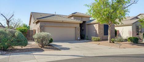 A two-story house with a garage, a driveway, and a well-maintained front yard with various shrubs and a tree.
