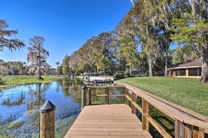A wooden dock extending over a calm body of water, surrounded by lush greenery and trees with Spanish moss.