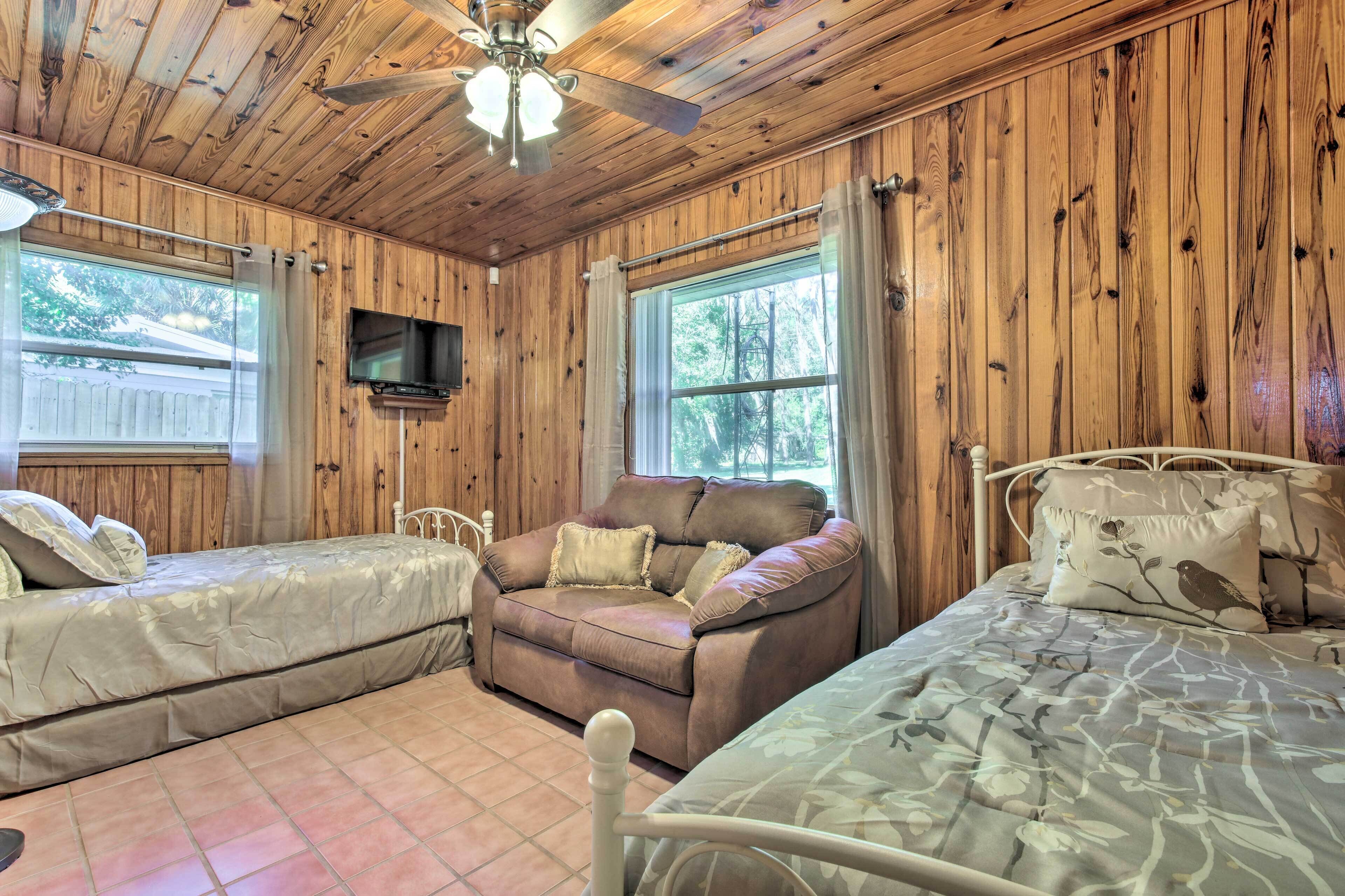 A cabin with wooden walls, a ceiling fan, a sofa, two beds, and a TV.