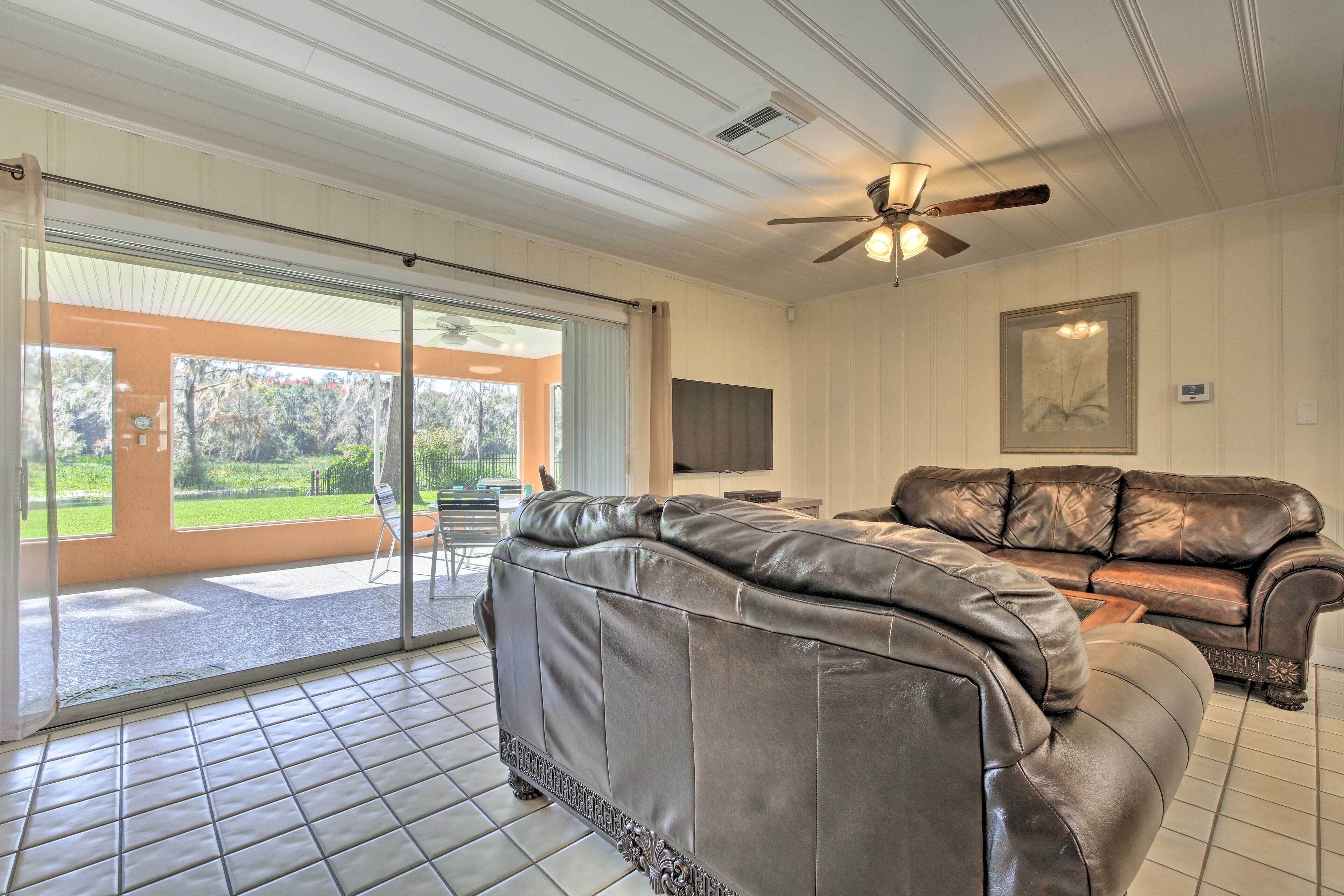 A spacious living room with a large leather sofa, a ceiling fan, and a sliding glass door leading to a patio.