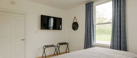 Ein Schlafzimmer mit Bett, Deckenventilator, an der Wand montiertem Fernseher und einem Fenster mit Vorhängen.