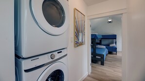 A laundry area with stacked washing machines, a bunk bed room visible through an open door, and a modern light fixture. - Modern Family Home in Mason w/ Backyard + Fire Pit (Mason)