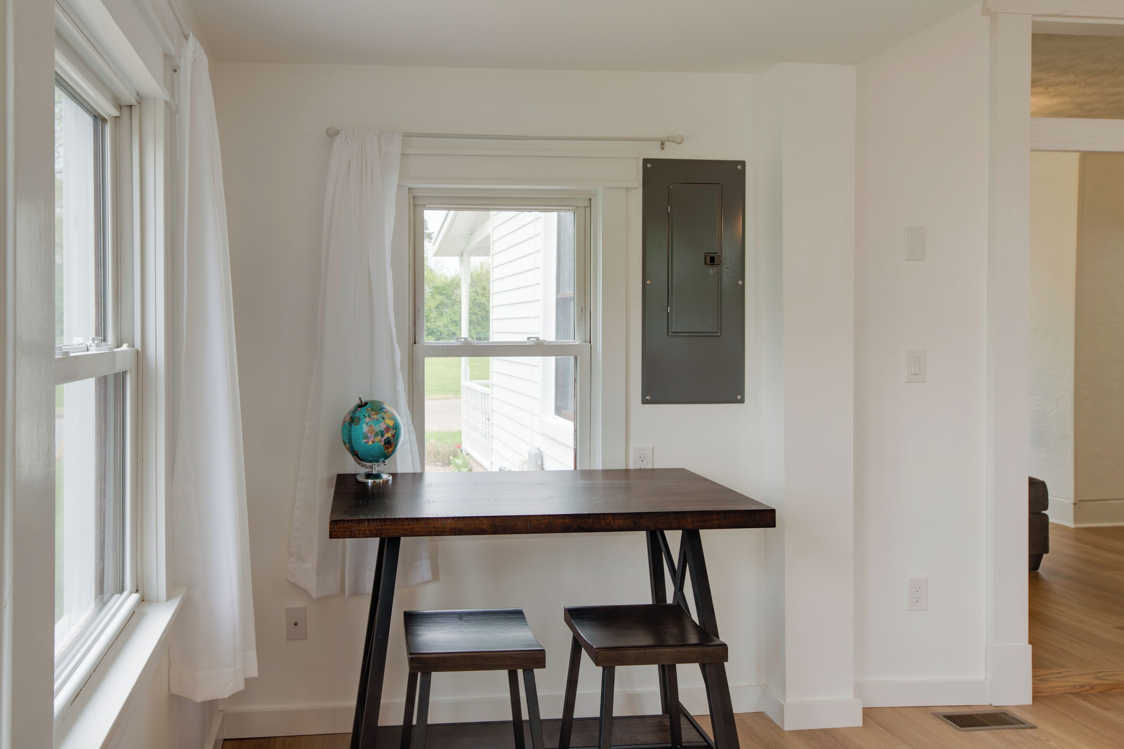 A room with a wooden table and two stools, a globe on the table, and a window with curtains.