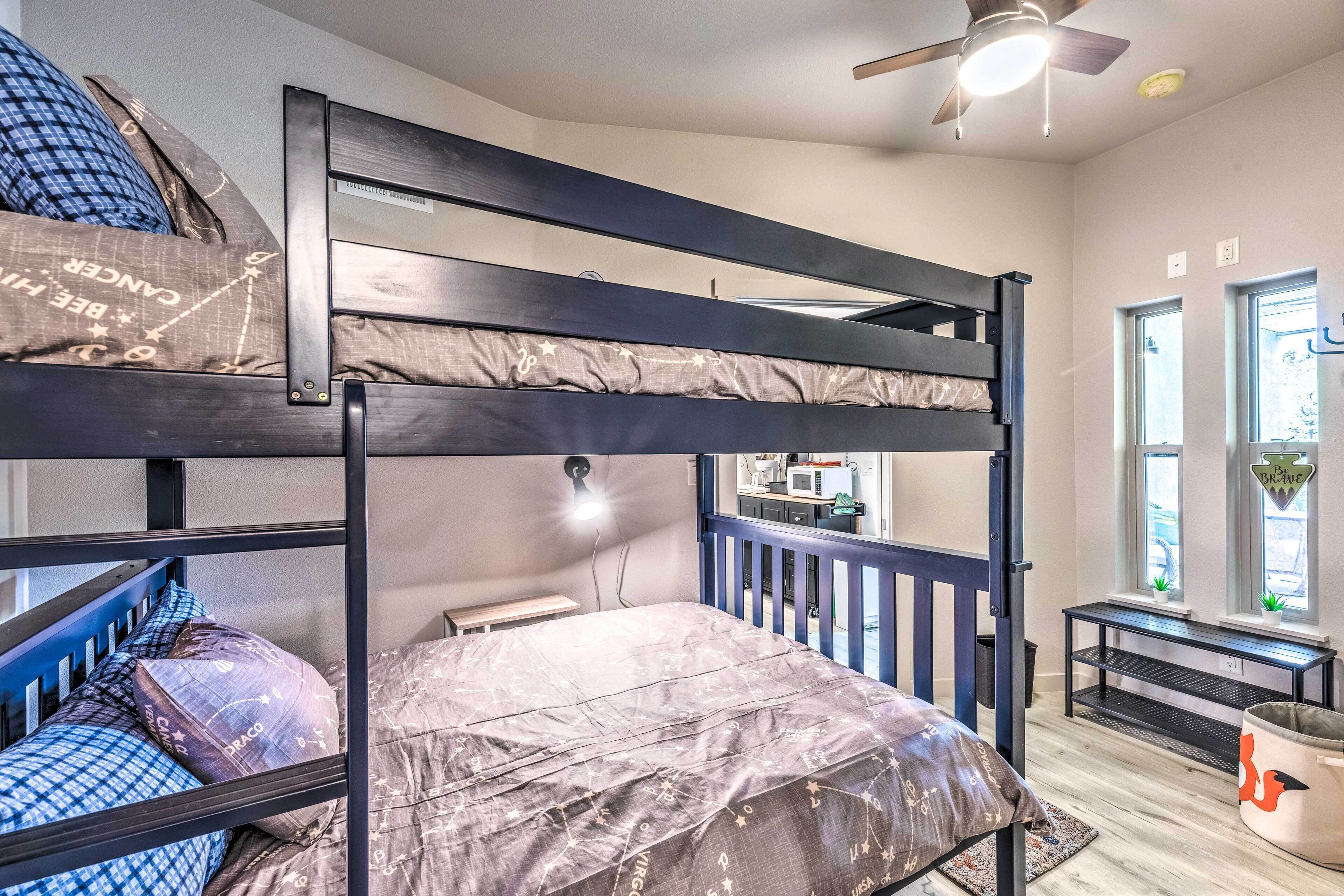 A bunk bed room with a ceiling fan, a desk, and a window with a view.