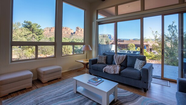 Un salon spacieux doté de grandes fenêtres, d’un canapé gris, d’une table basse blanche et offrant une vue sur un paysage montagneux.