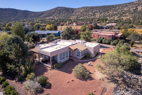 Una casa moderna con un patio amplio, rodeada por un paisaje árido y rocoso con vegetación escasa.
