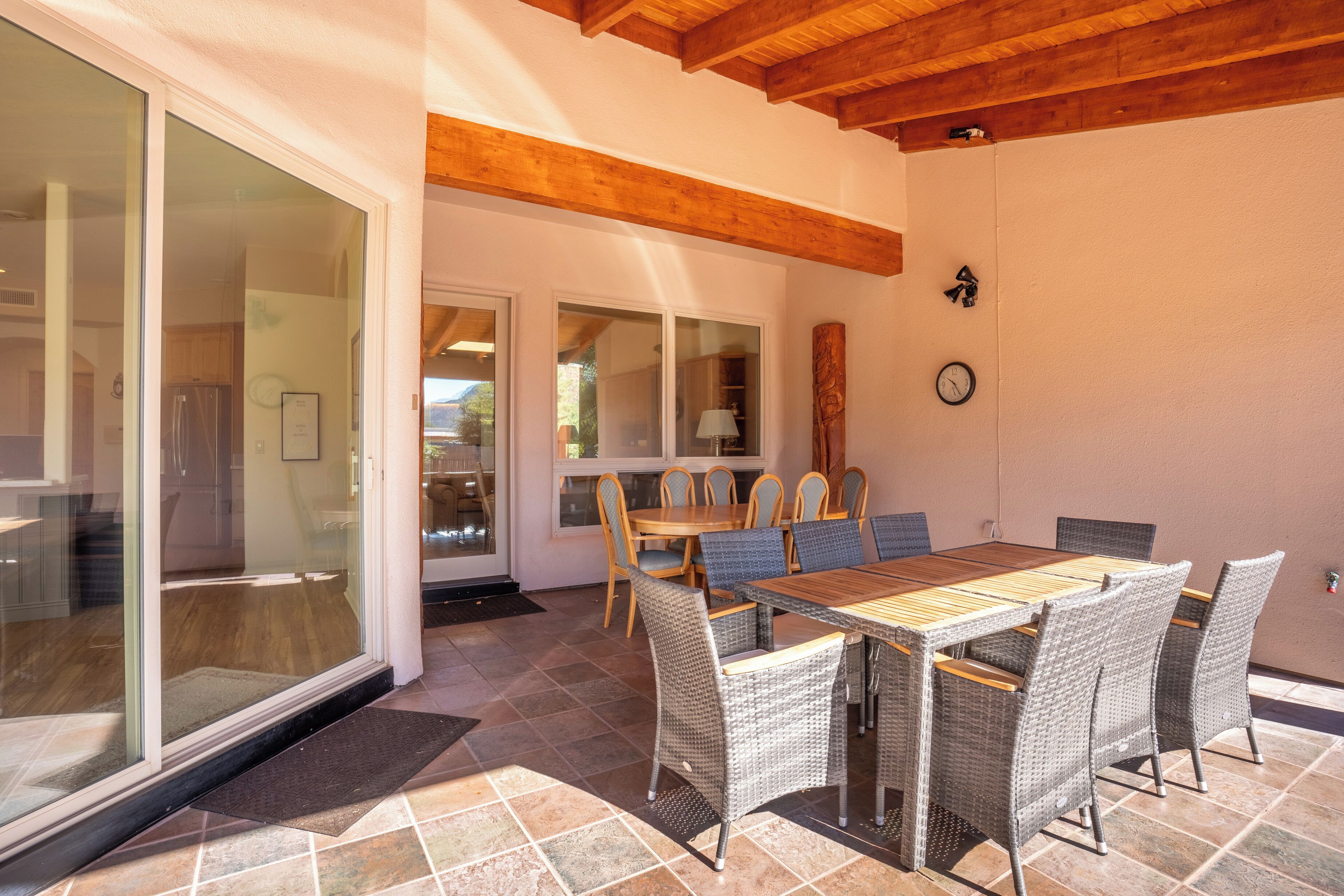A dining area with a wooden table and wicker chairs, a sliding glass door leading to a kitchen, and a wooden ceiling.