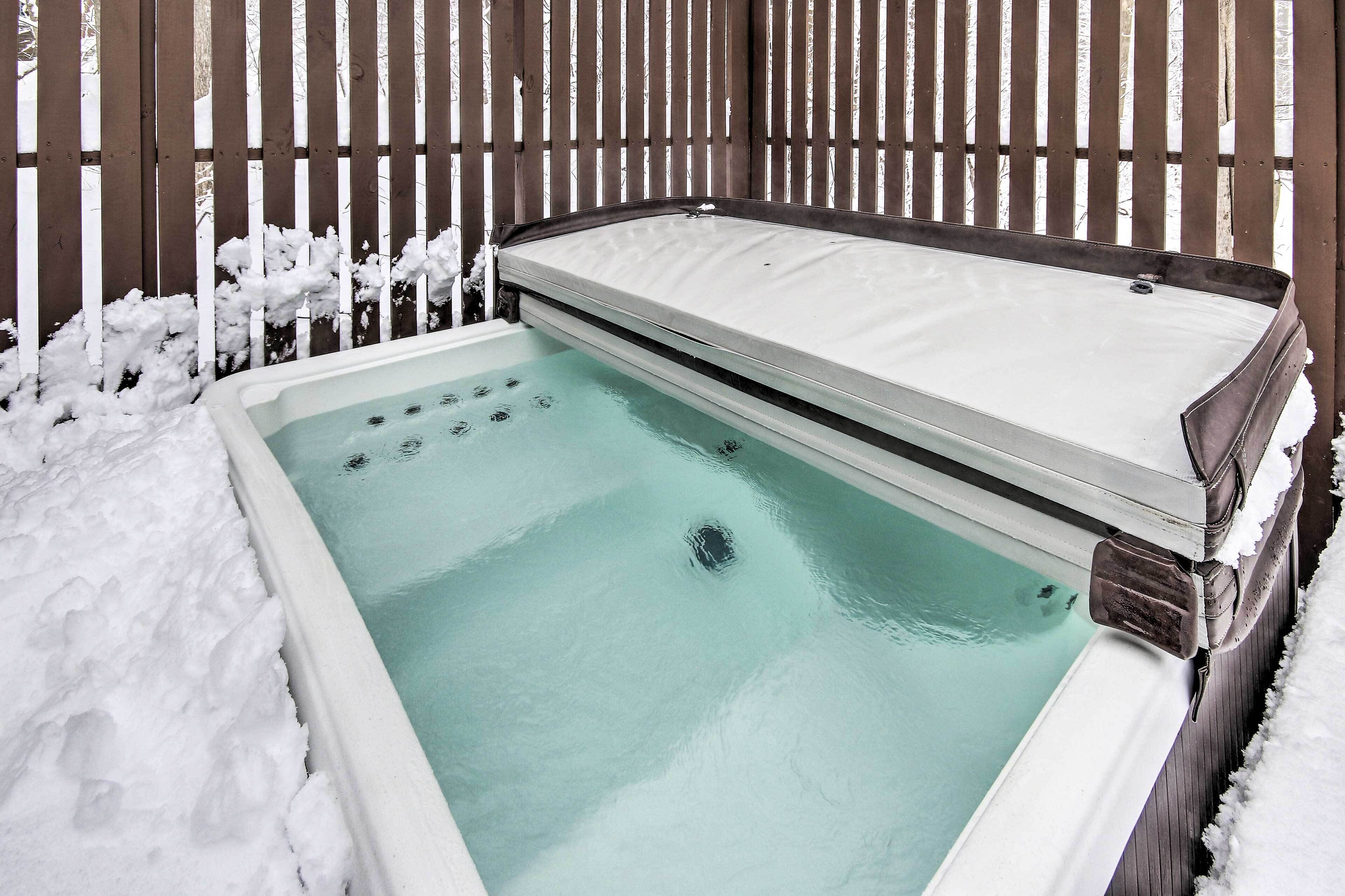 A hot tub with a wooden deck and snow accumulation around it.