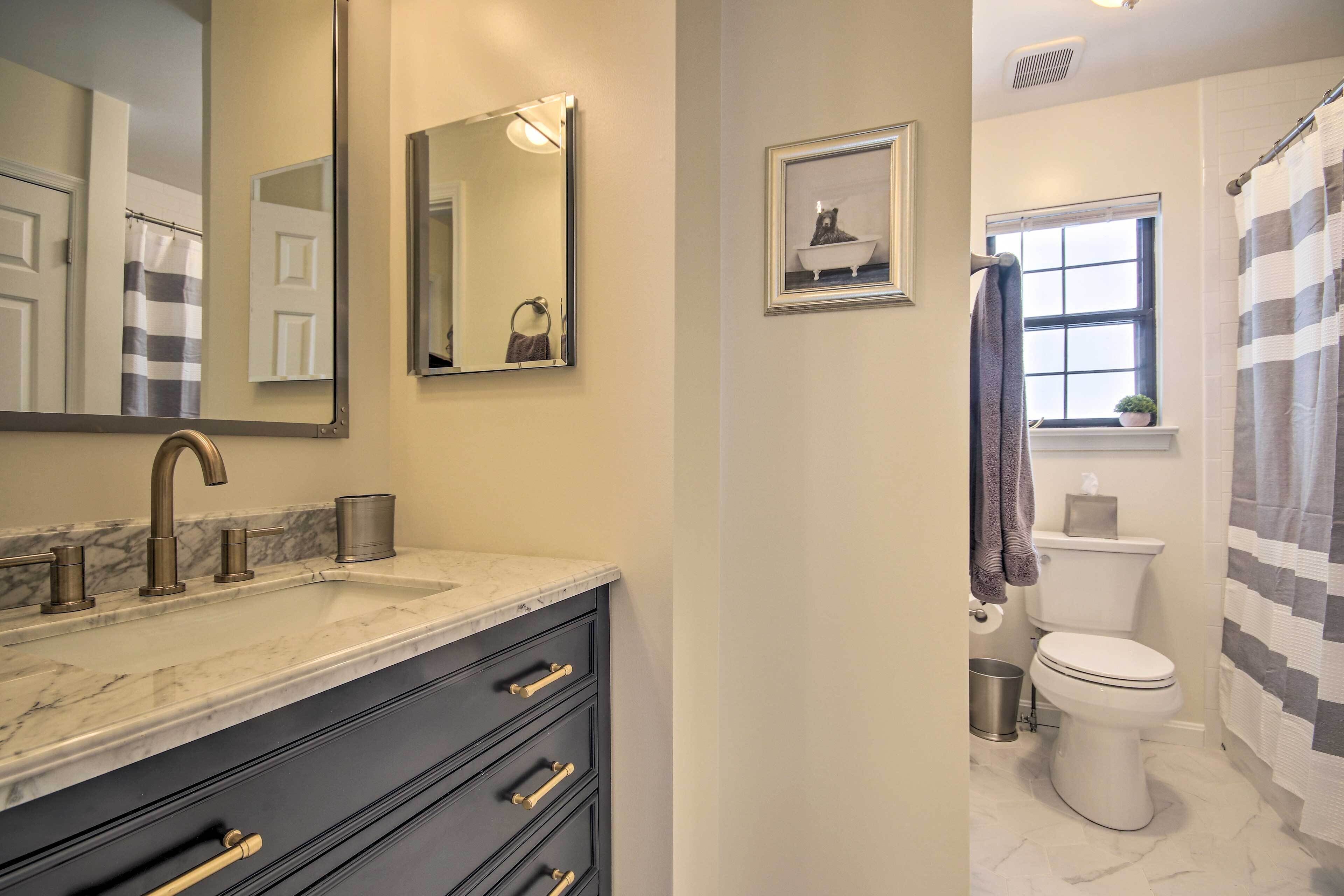 A bathroom with a marble sink, a toilet, a shower curtain, and a framed picture on the wall.