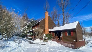 Una casa de dos pisos con una chimenea de ladrillo, un techo cubierto de nieve y una valla de madera.