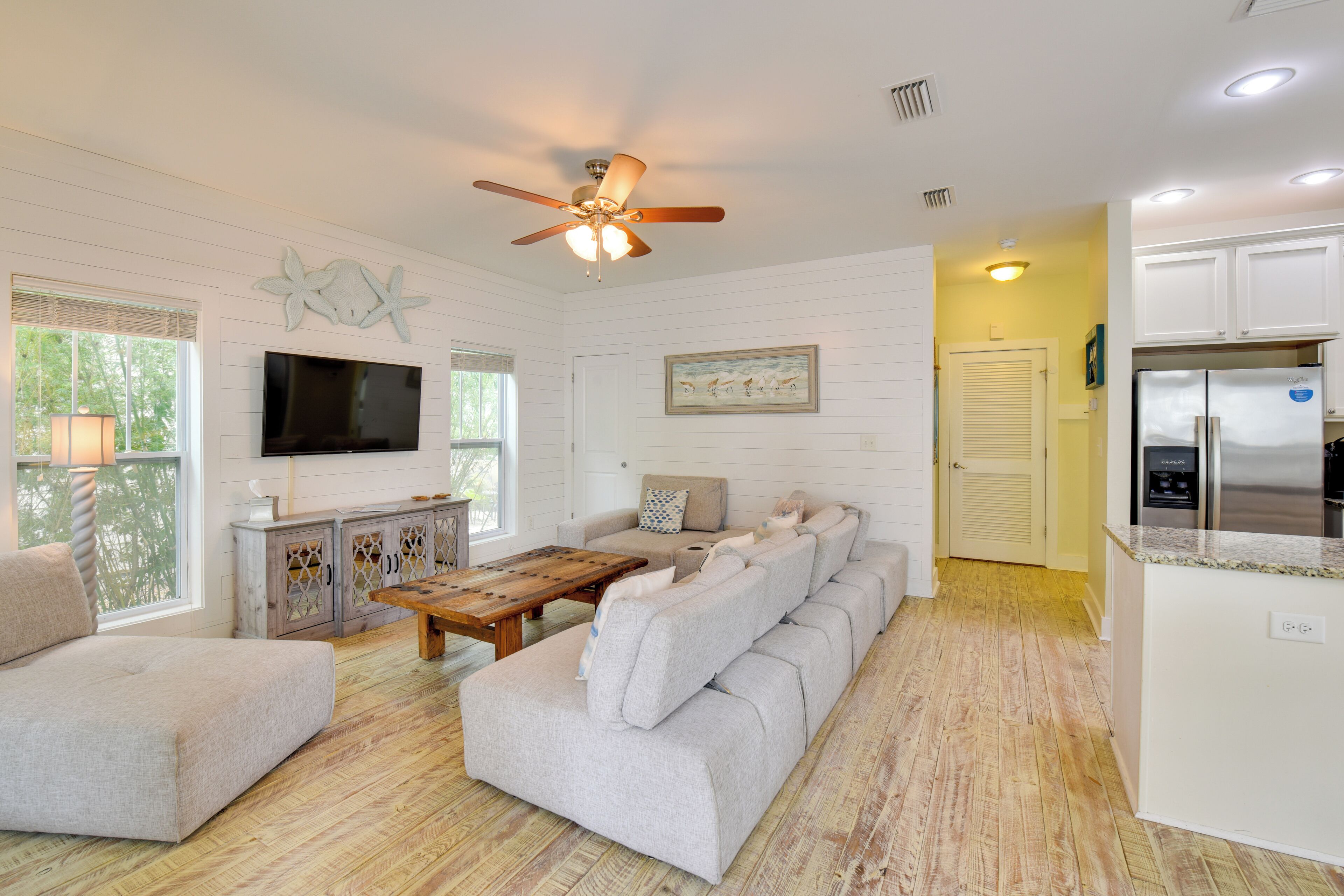 A spacious living room with a large sofa, a wooden coffee table, and a flat-screen TV mounted on the wall.