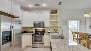 A modern kitchen with white cabinetry, stainless steel appliances, granite countertops, and a dining area with wooden chairs. - Sunny Santa Rosa Beach in 30 A Neighborhood! (Santa Rosa Beach)