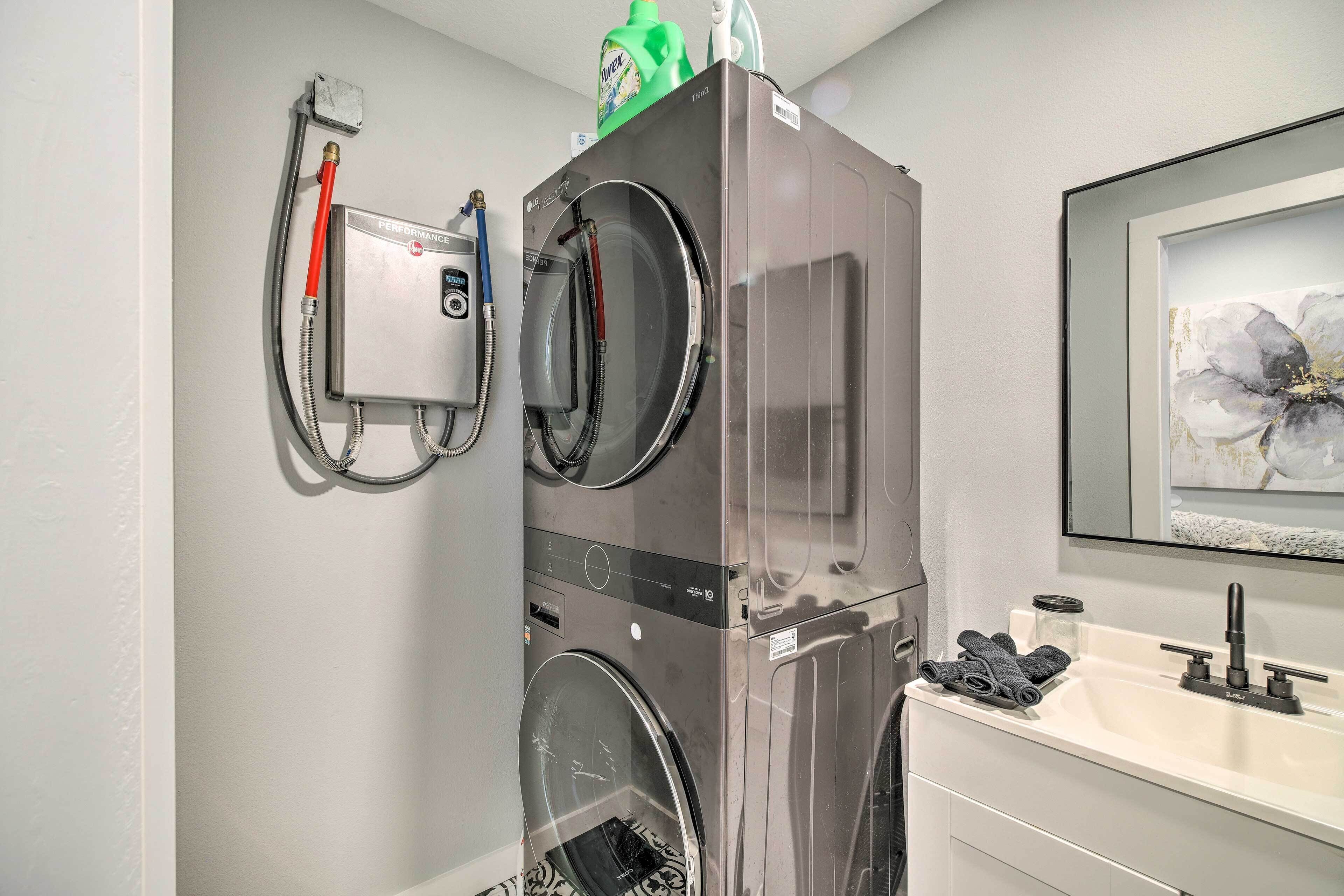 A compact, modern laundry room with a built-in washer and dryer, a small sink with a faucet, and a framed artwork above the sink.
