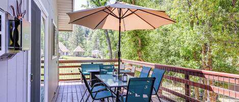 An outdoor deck with a table and chairs, a large umbrella, and a view of trees.