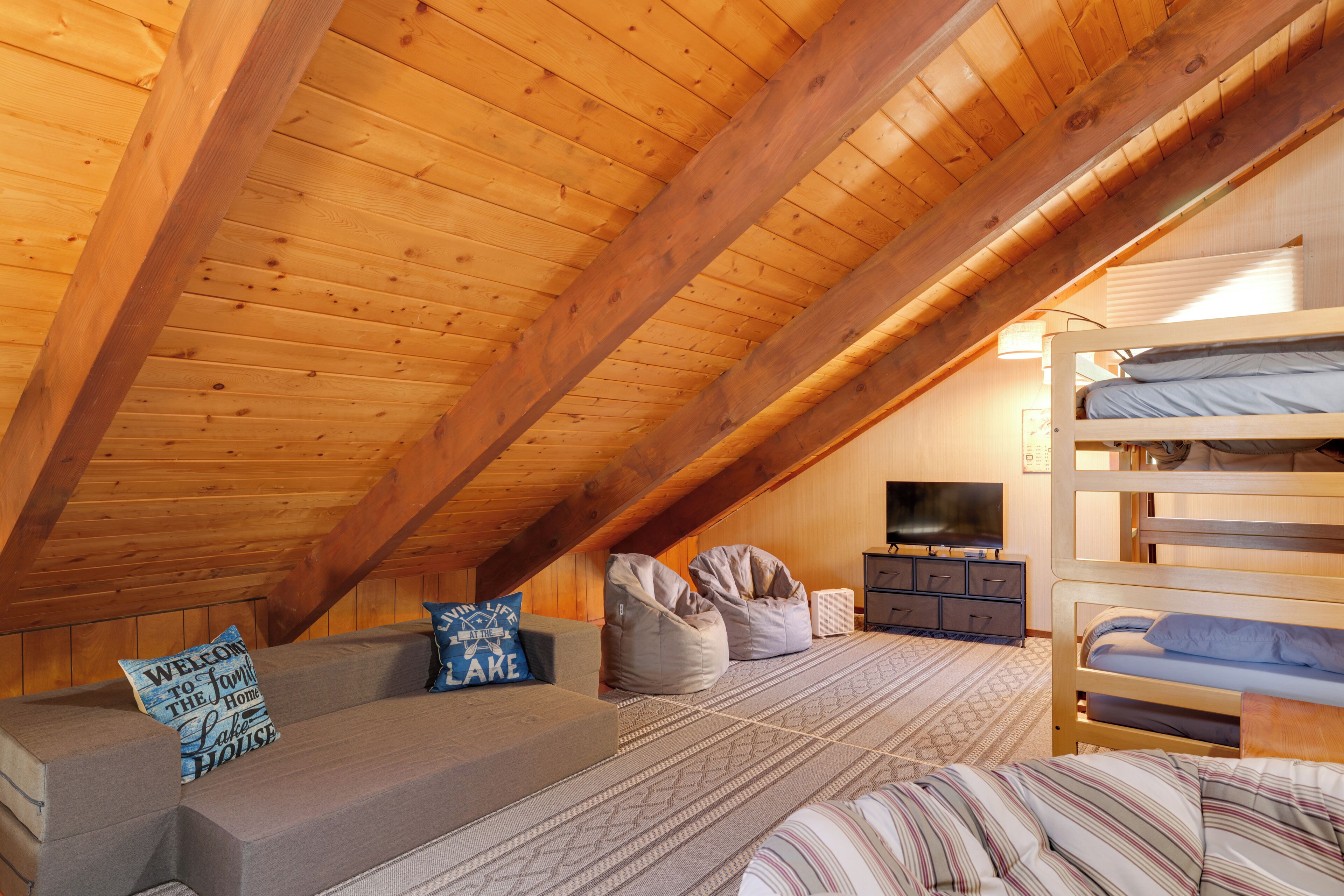 A cozy attic bedroom with a wooden ceiling, bunk beds, a sofa, and a television.