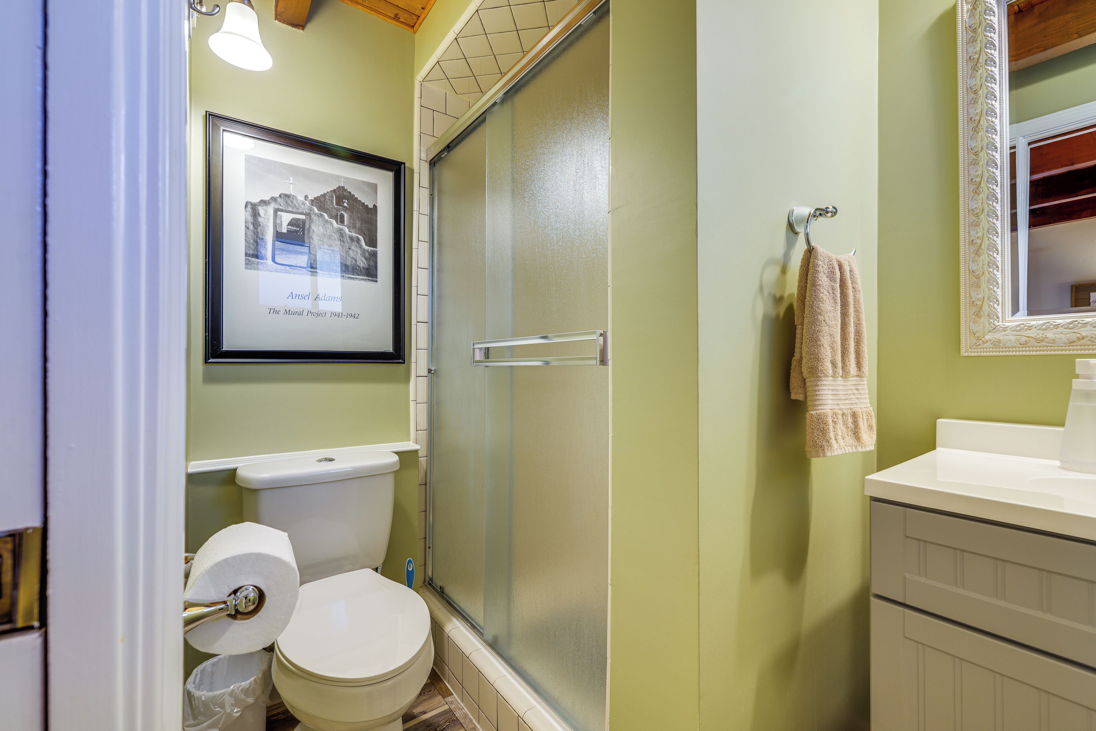 A bathroom with a toilet, a framed picture on the wall, a towel hanging on a rack, and a mirror with an ornate frame.