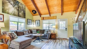 A cozy living room with a sectional sofa, a round coffee table, and a television on a wooden cabinet. - Groveland Home - Walk to Pine Mountain Lake! (Groveland)