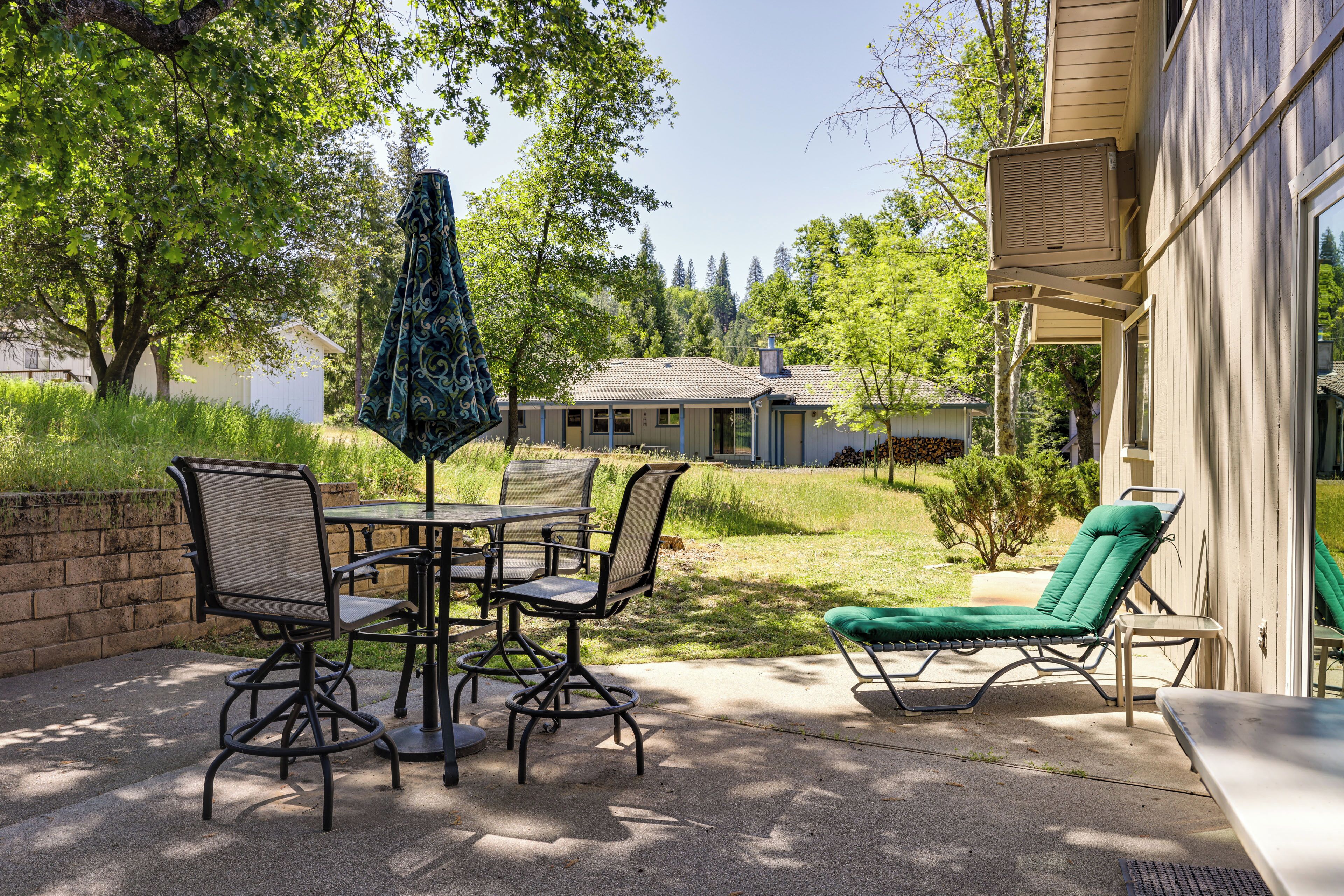 An outdoor patio with a table and chairs, a green cushioned lounge chair, and a patio umbrella.