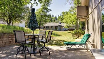 An outdoor patio with a table and chairs, a green cushioned lounge chair, and a patio umbrella.