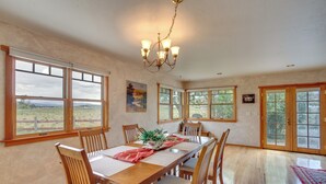 Ein Esszimmer mit einem langen Holztisch, Stühlen und einer Chandelüster. Große Fenster bieten Blick ins Freie.