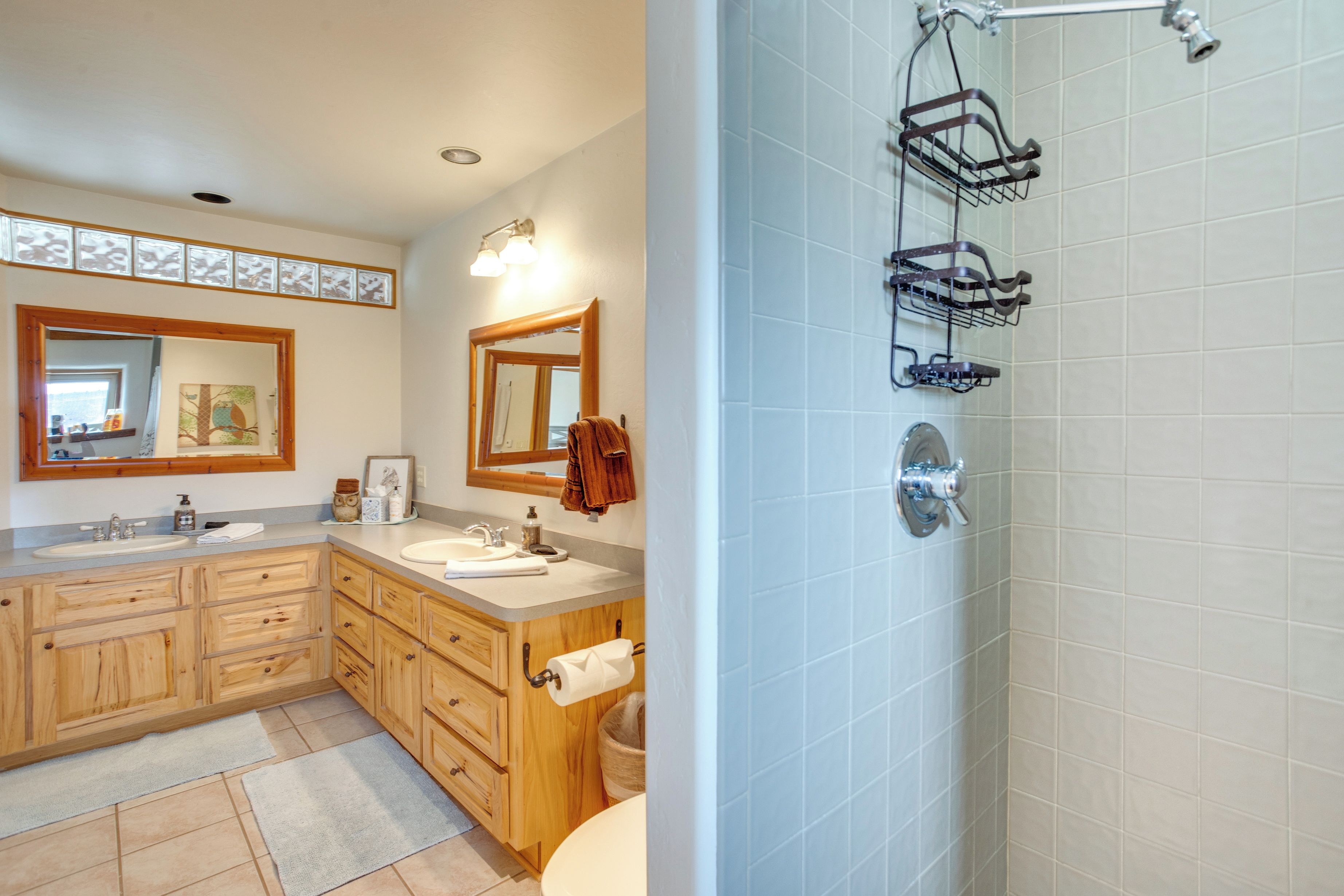 A bathroom with wooden cabinets, a double sink, a large mirror, and a shower area with a metal rack.