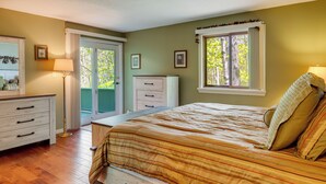 Een slaapkamer met een bed, een dressoir en een raam met uitzicht op bomen.