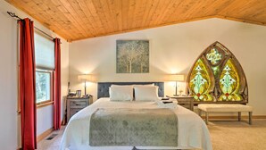 A bedroom with a large bed, wooden ceiling, stained glass window, and a painting on the wall. - Secluded Leesburg Retreat w/ Private Hot Tub! (Leesburg)