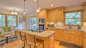 A modern kitchen with wooden cabinets, a central island with bar stools, stainless steel appliances, and large windows offering a view of the outdoors. - Secluded Leesburg Retreat w/ Private Hot Tub! (Leesburg)