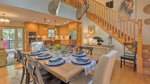 A spacious dining area with a wooden table set for six, a staircase with wooden railings, and a kitchen in the background. - Secluded Leesburg Retreat w/ Private Hot Tub! (Leesburg)
