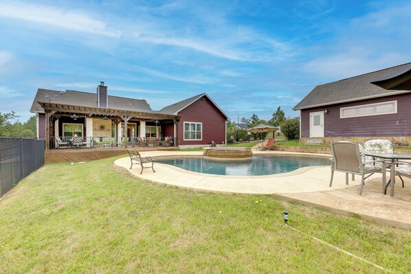A residential backyard with a swimming pool, patio furniture, and a covered outdoor seating area.