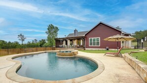 A backyard with a swimming pool, a wooden deck, and a house with a red exterior. - Pool & Hot Tub in Sunny Smithville Getaway! (Smithville)