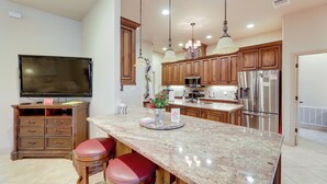 A kitchen with wooden cabinets, a granite countertop, stainless steel appliances, and a flat-screen TV. - Pool & Hot Tub in Sunny Smithville Getaway! (Smithville)