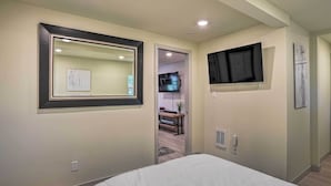 Une chambre d’hôtel avec un grand lit, un téléviseur fixé au mur, un miroir et une porte donnant sur une petite cuisine.